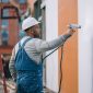 worker painting wall with spray gun white color 85x85
