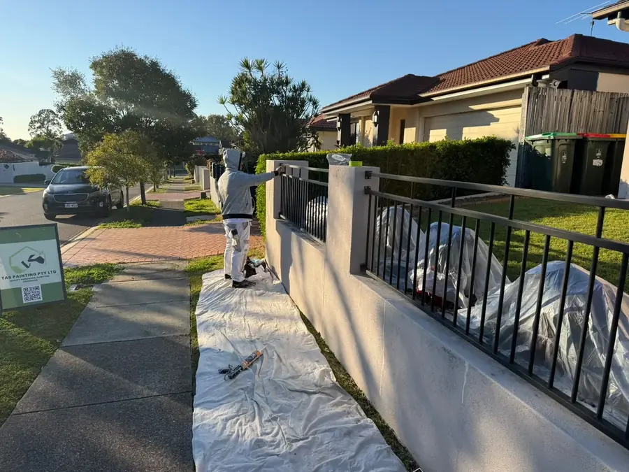 Painter coating a front fence and balustrade beside a driveway