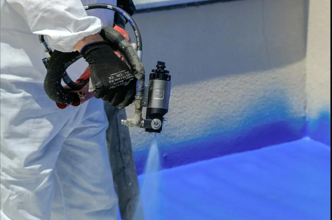 Professional spray gun applying blue paint to a wall